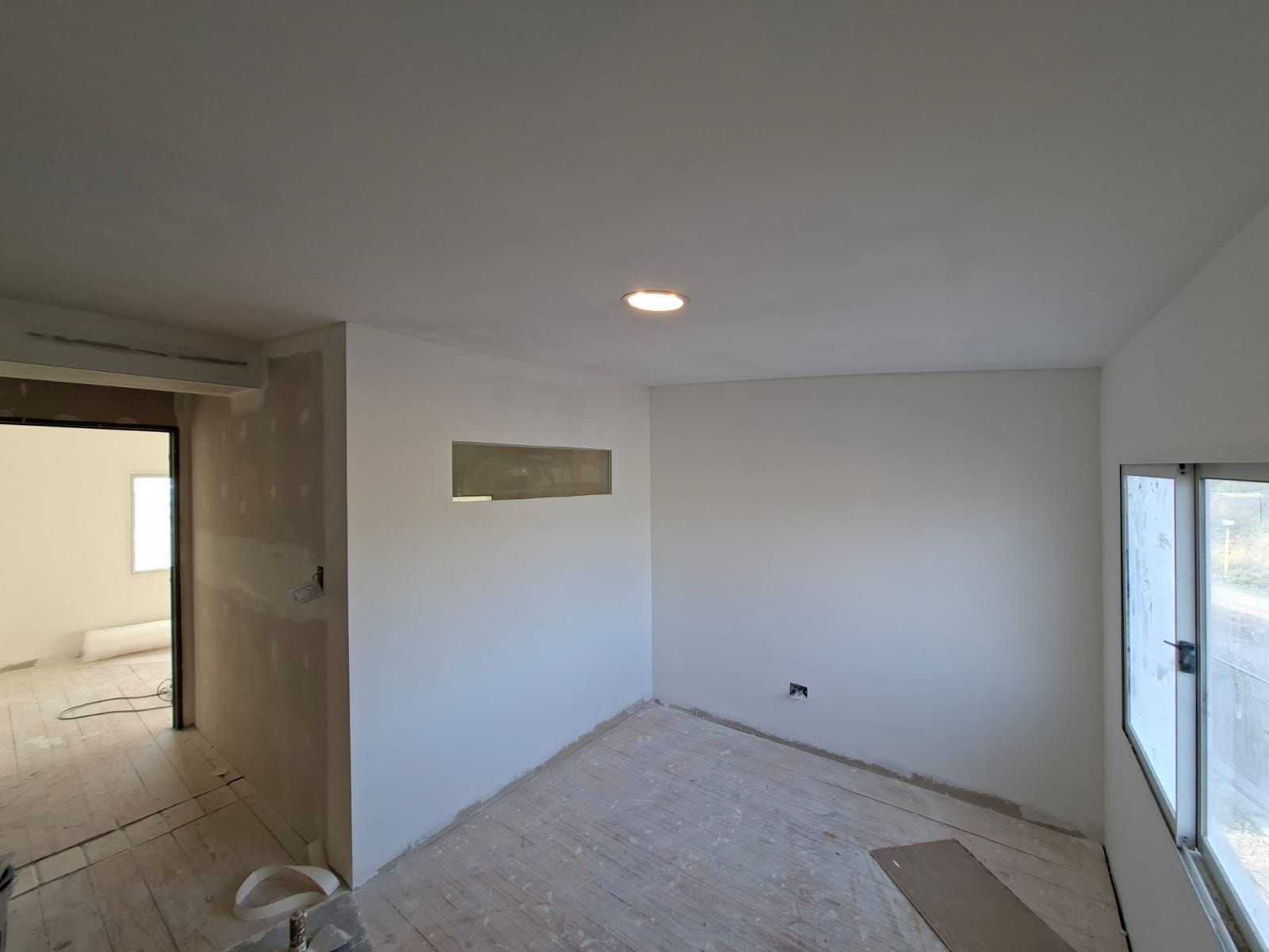 Habitación interior con paredes blancas, una ventana y una puerta abierta; en proceso de renovación.