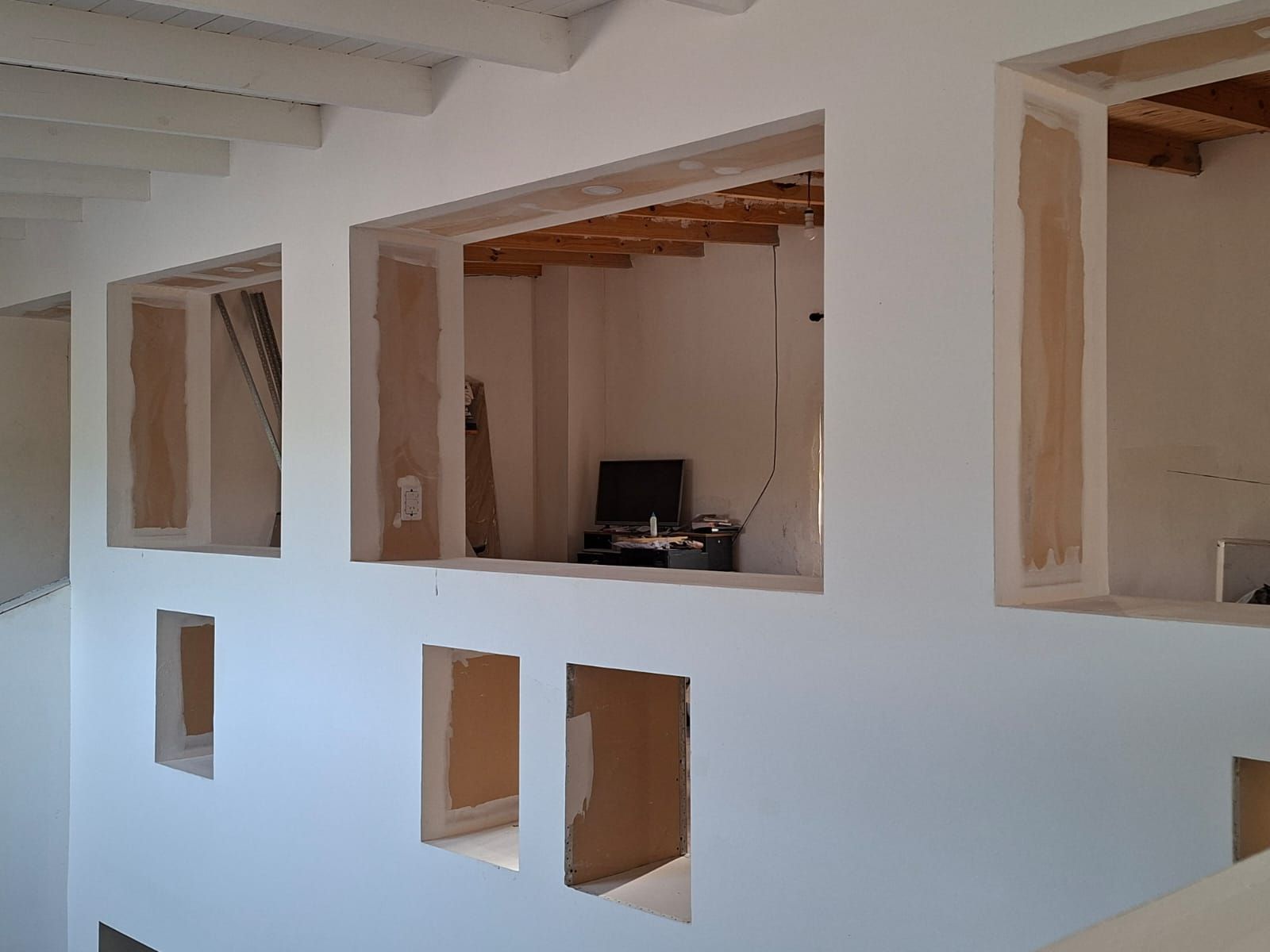 Pared blanca con recortes rectangulares; algunos tienen marcos de madera a la vista, otros dan acceso a una habitación.