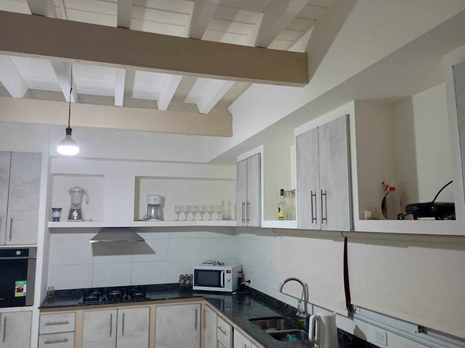 Cocina con gabinetes blancos, encimeras negras, estufa, microondas y vigas a la vista.