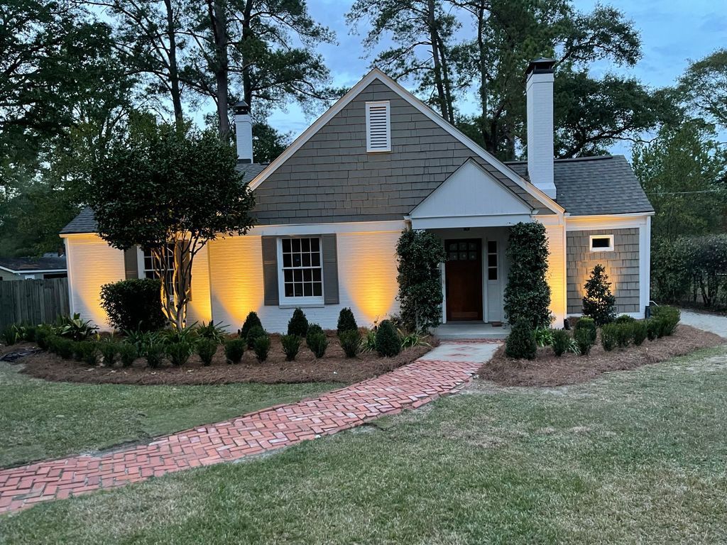 Charming cottage with lit exterior, brick walkway, and landscaped yard at dusk