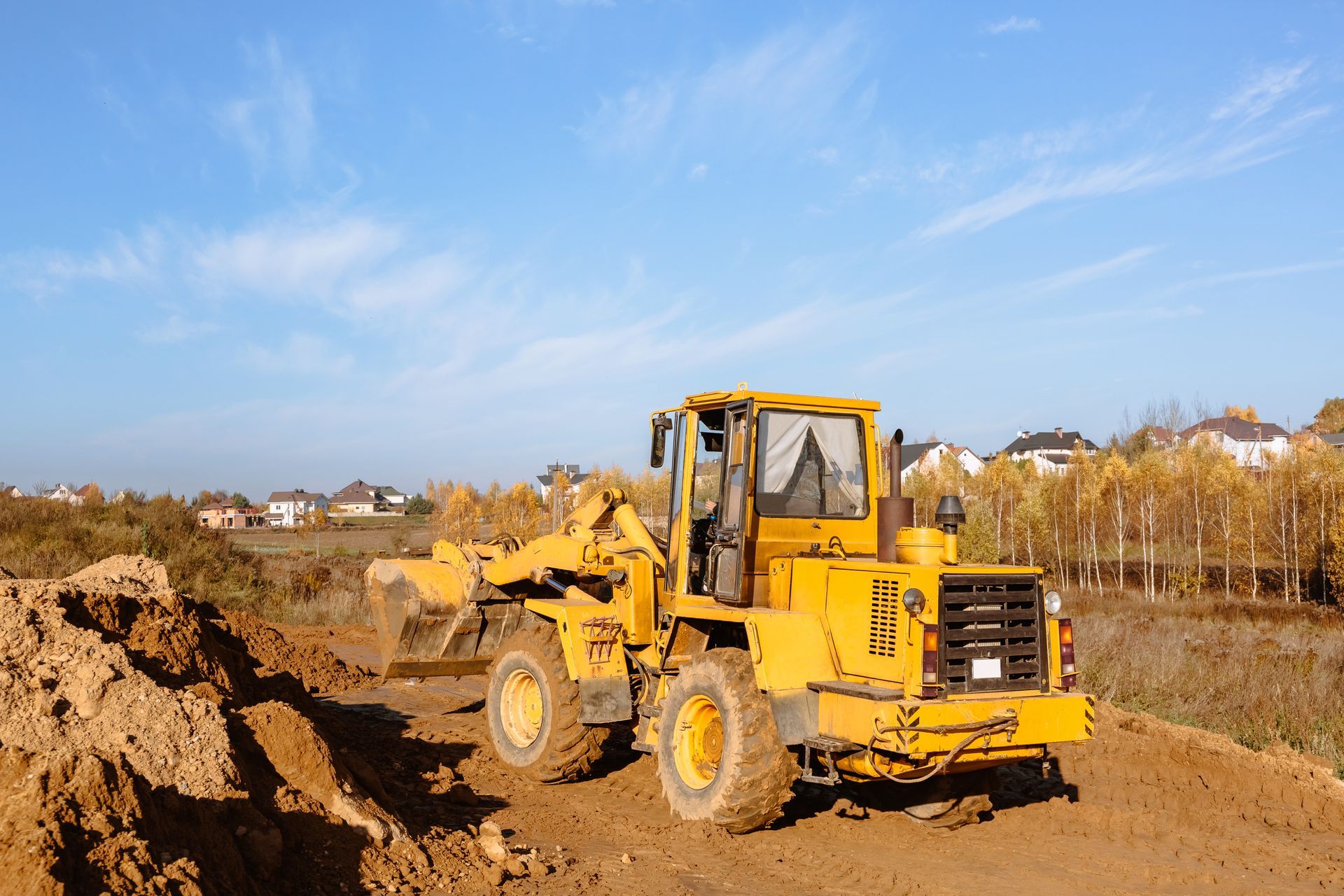 A big yellow wheel loader prepares a plot of land for a new structure, grading the ground and adding sand for building.