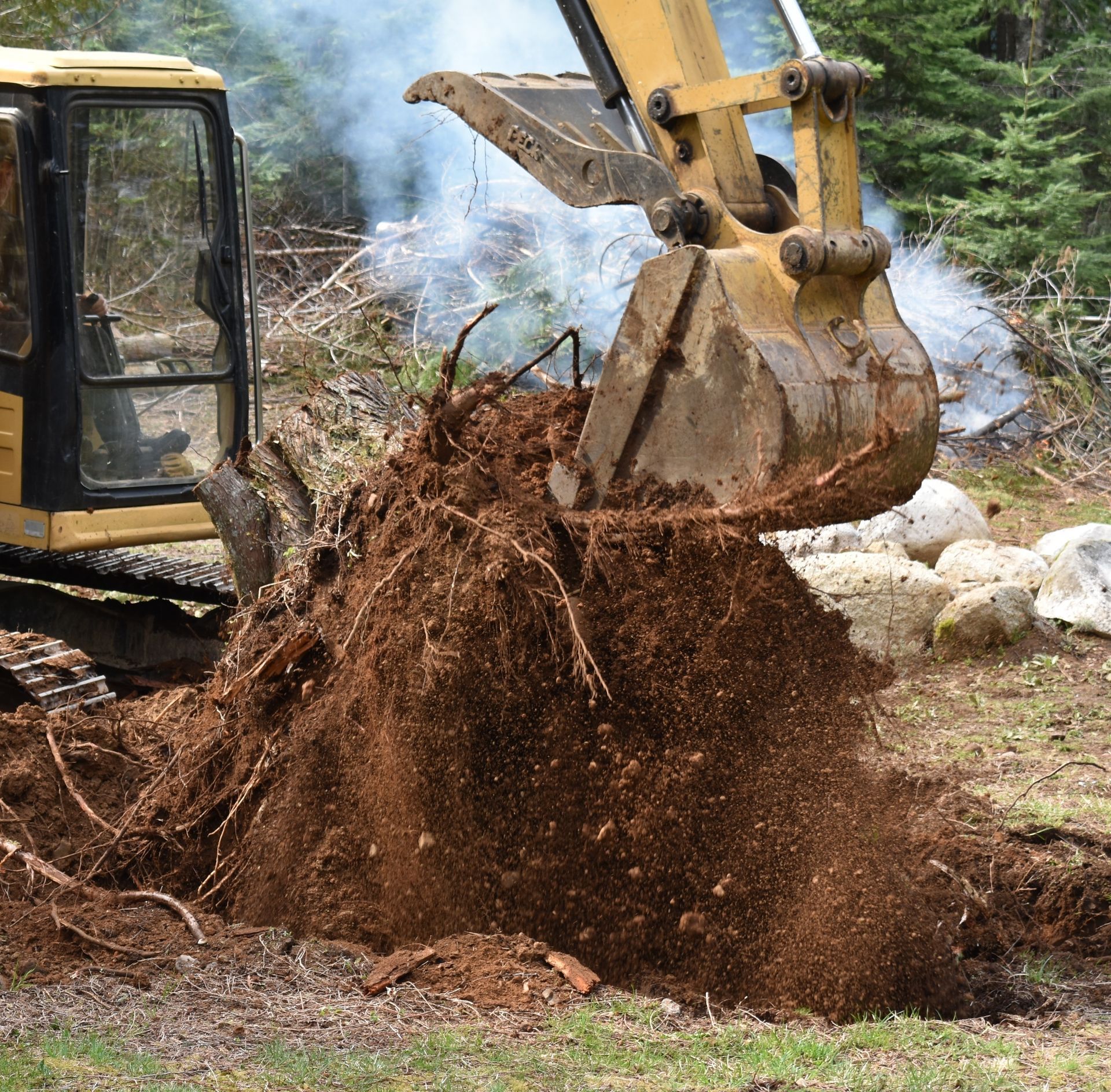 An excavator is removing a tree stump as part of a lot clearing operation.