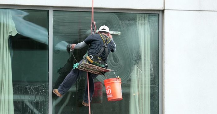Man Cleaning Outside Windows Of A Building While Strapped — Professional Cleaners In Central Coast, NSW
