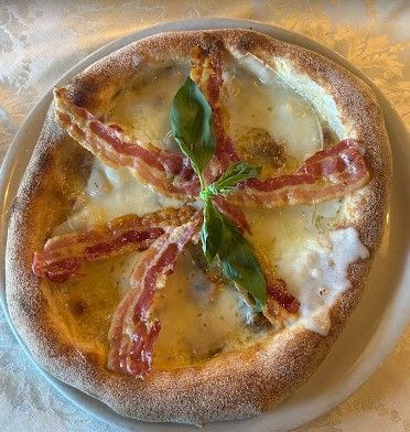 Una pizza con pancetta, formaggio e basilico su un piatto bianco.