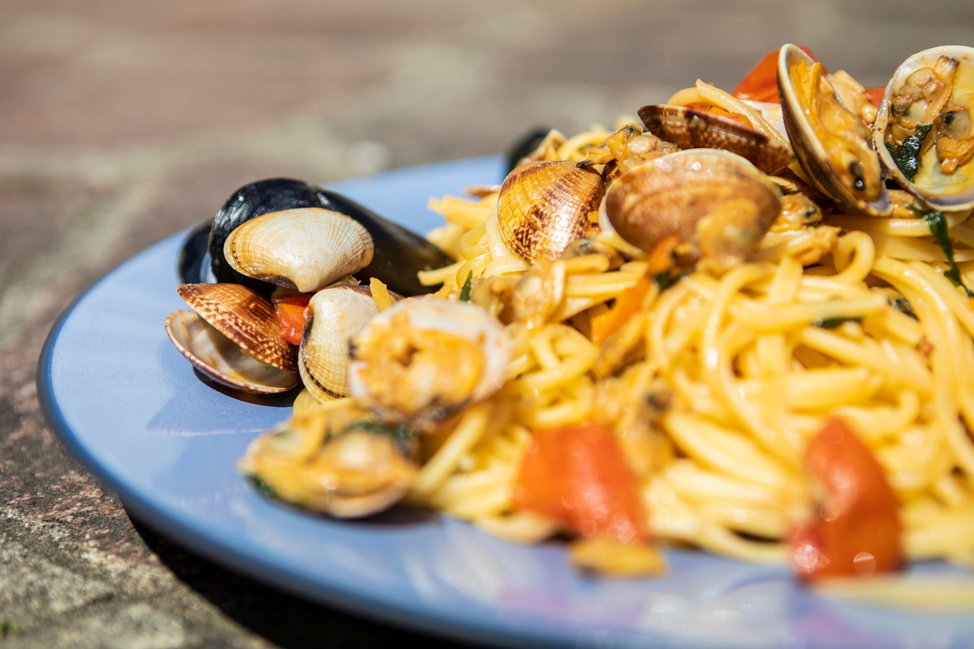 Un piatto blu con sopra tagliatelle, vongole e pomodori.