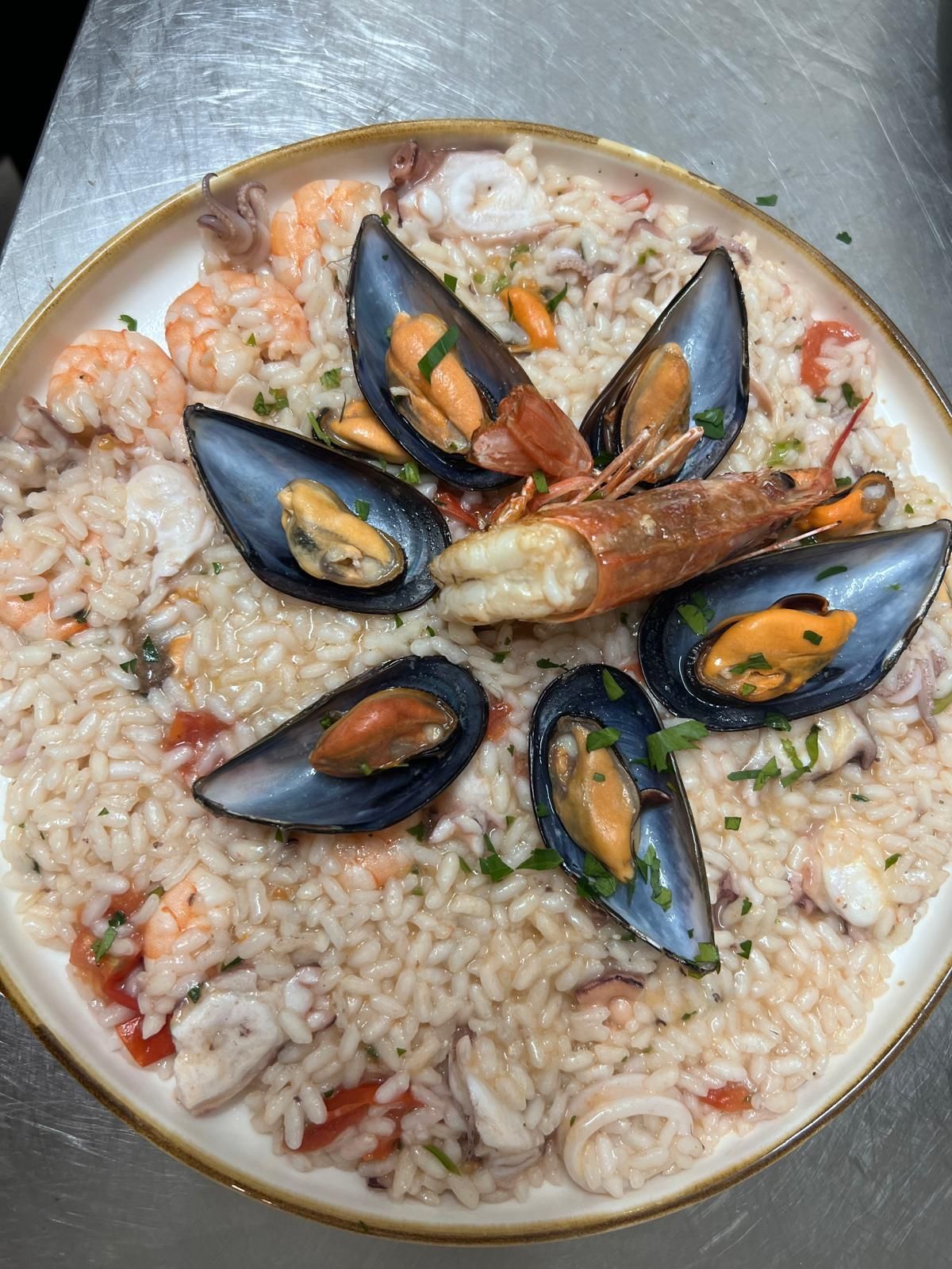 Un piatto blu con sopra tagliatelle, vongole e pomodori.