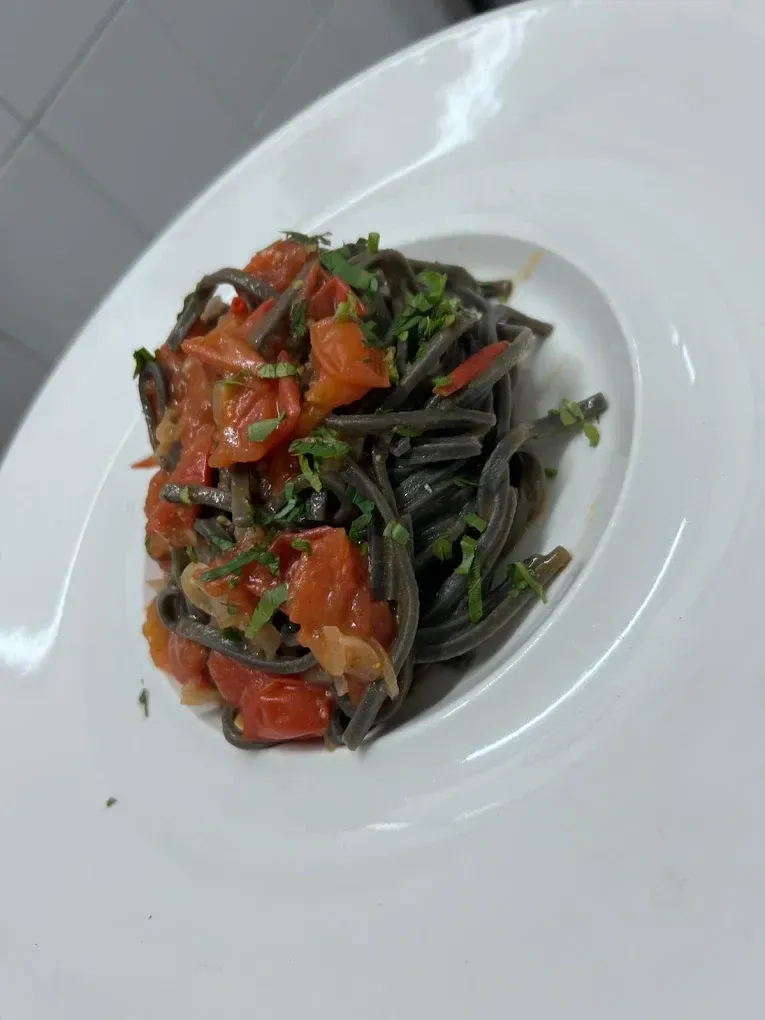 Un piatto bianco con sopra spaghetti e pomodori su un tavolo.