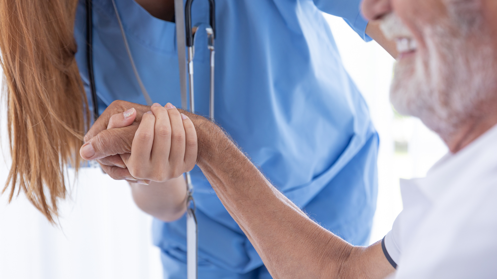 Healthcare worker holding an older patient's hand in a bright clinical setting