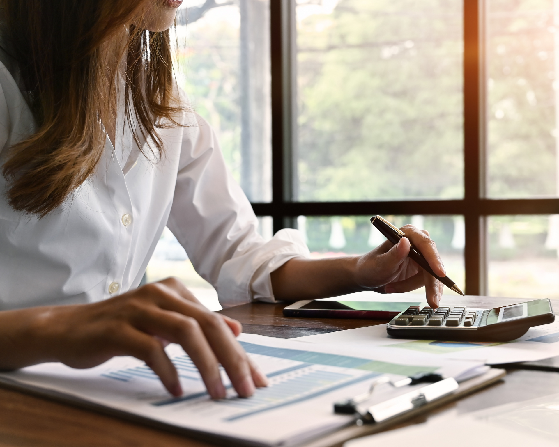 A woman is sitting at a desk using a calculator and a pen.