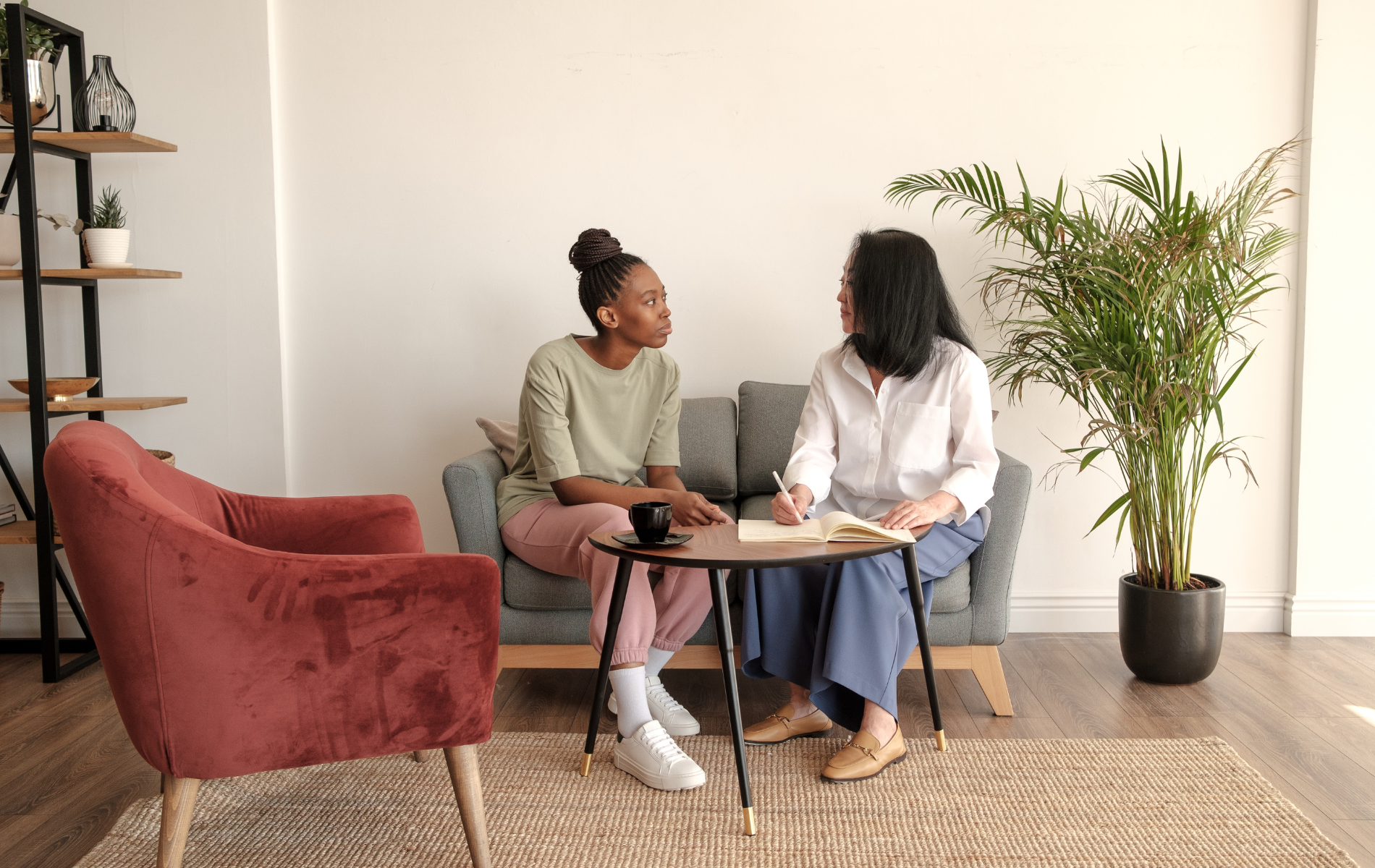 Two women are sitting on a couch talking to each other.