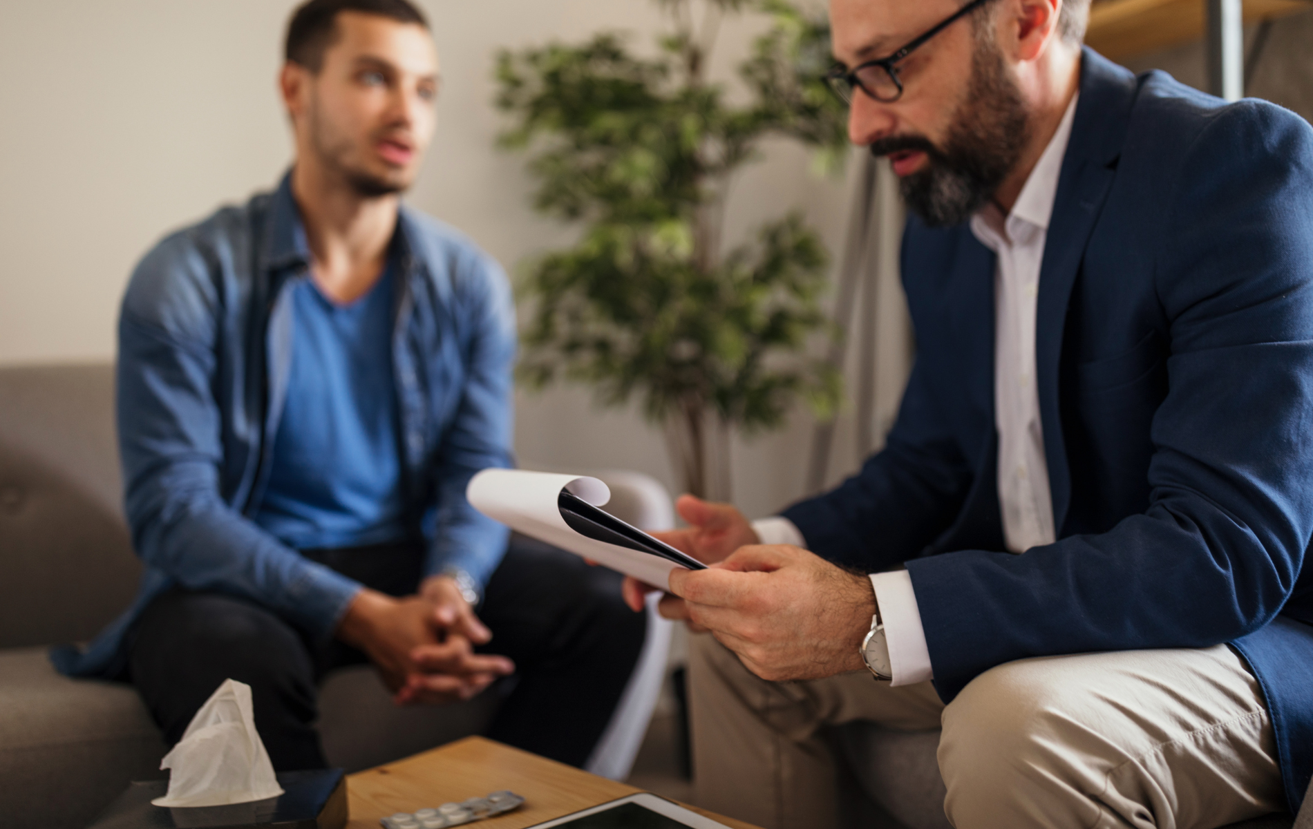 A man is sitting on a couch talking to a man in a suit.