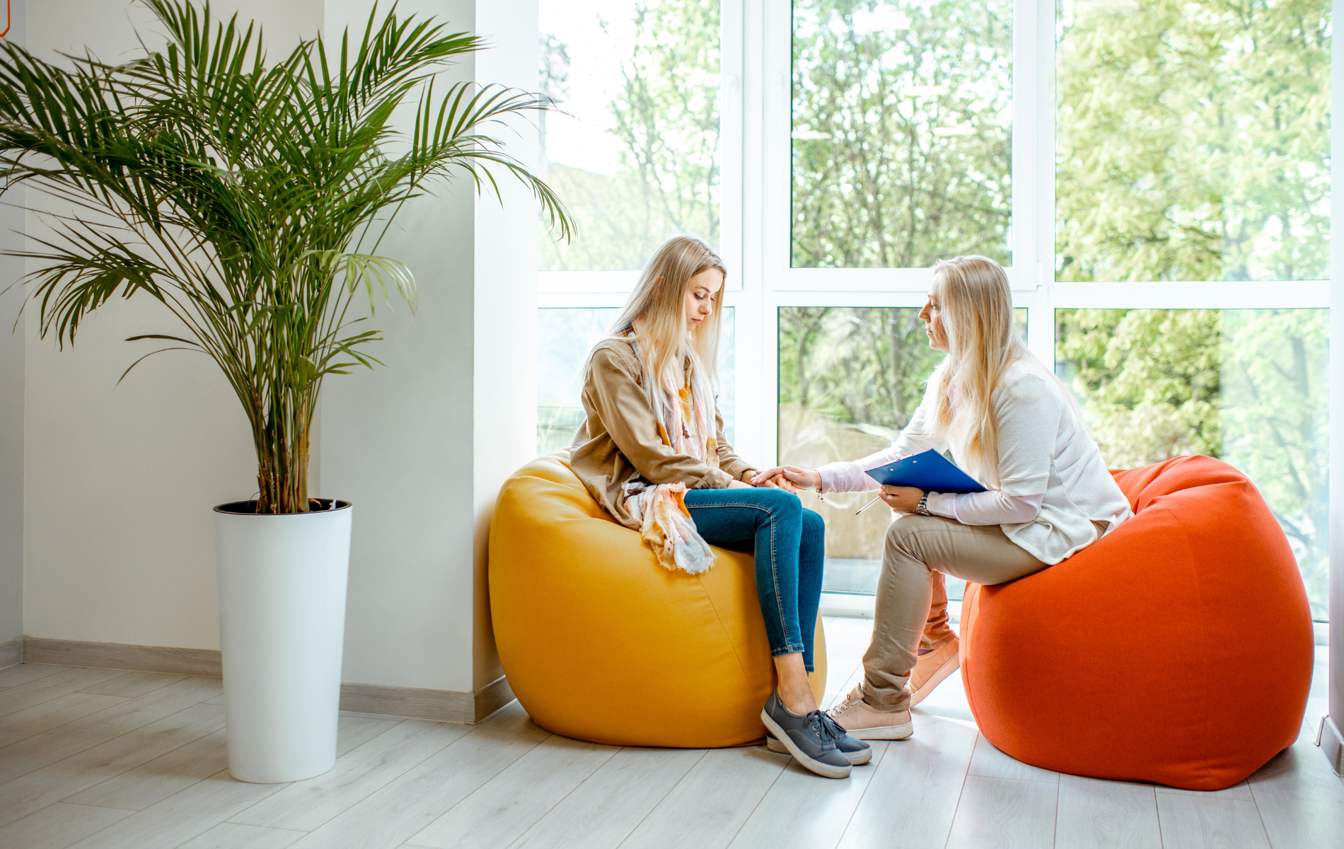 Two women are sitting on bean bag chairs in front of a window.