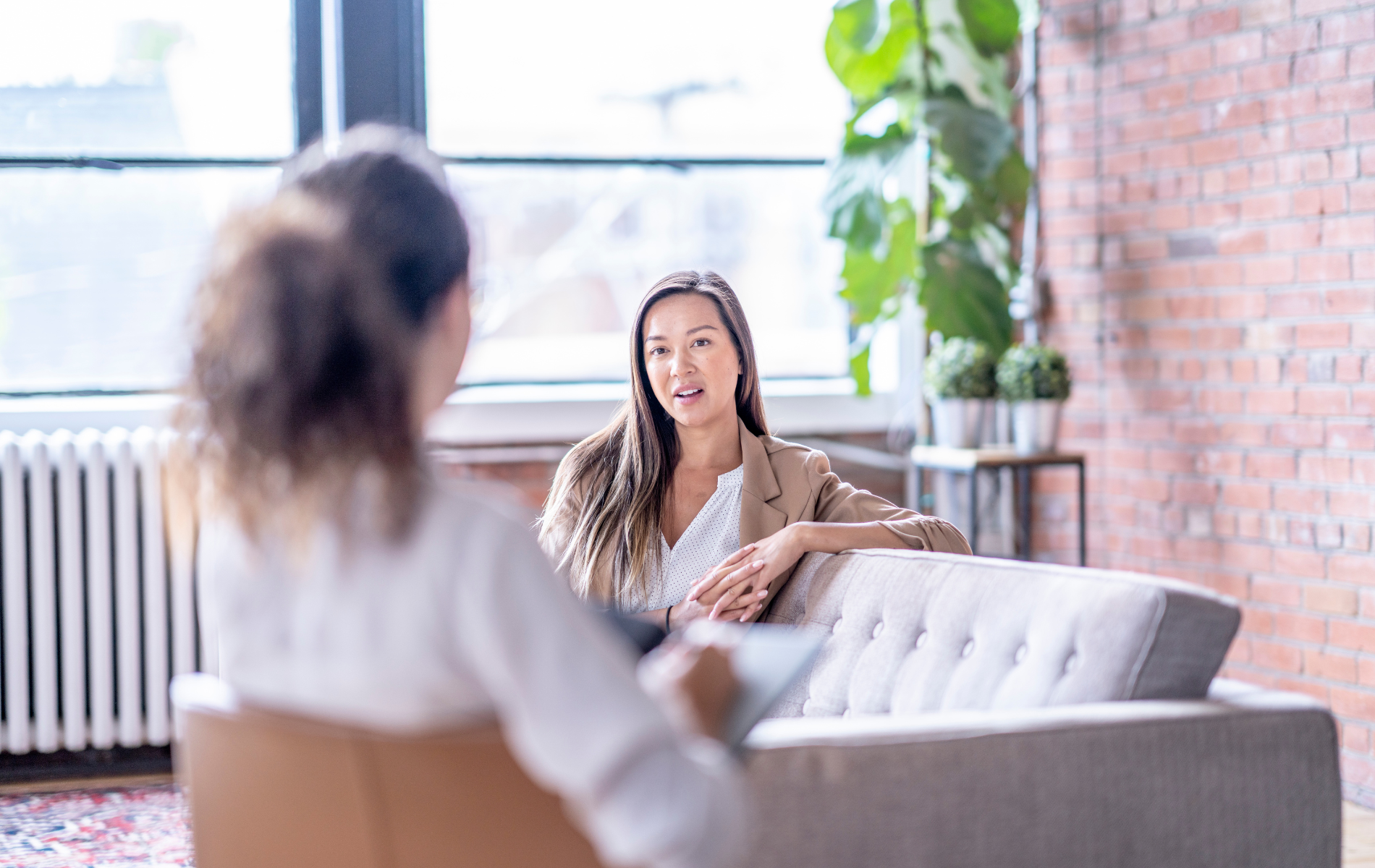A woman is sitting on a couch talking to another woman.