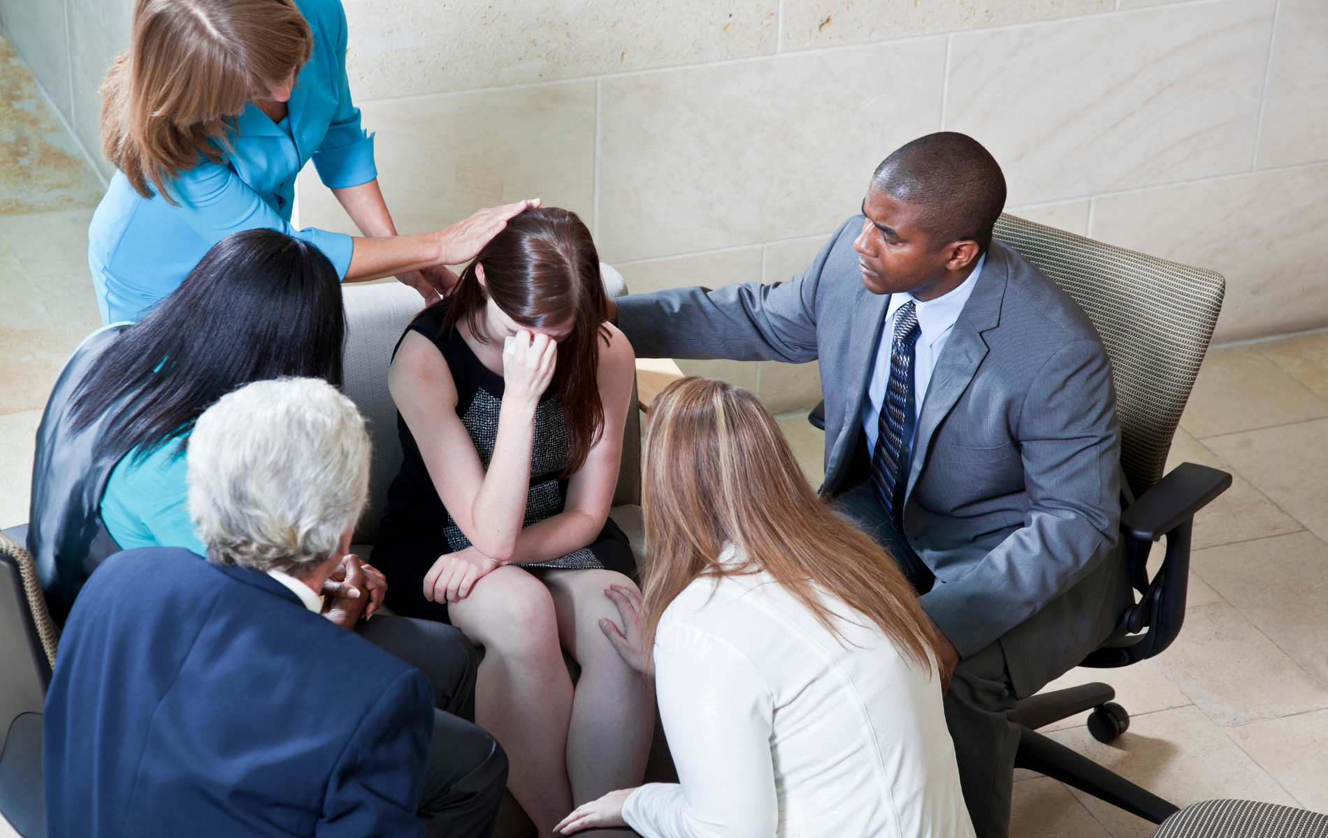 A group of people are sitting in a circle and a man is comforting a woman who is crying.