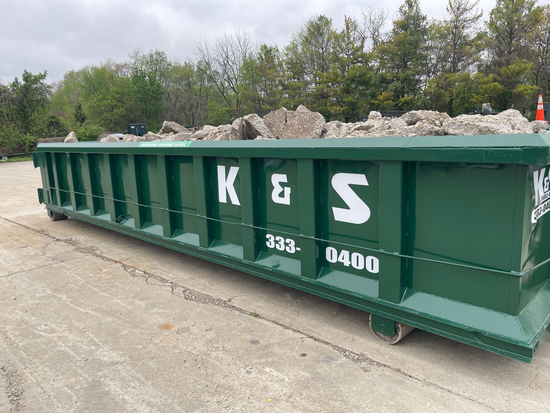 A large green dumpster is sitting on the side of the road.
