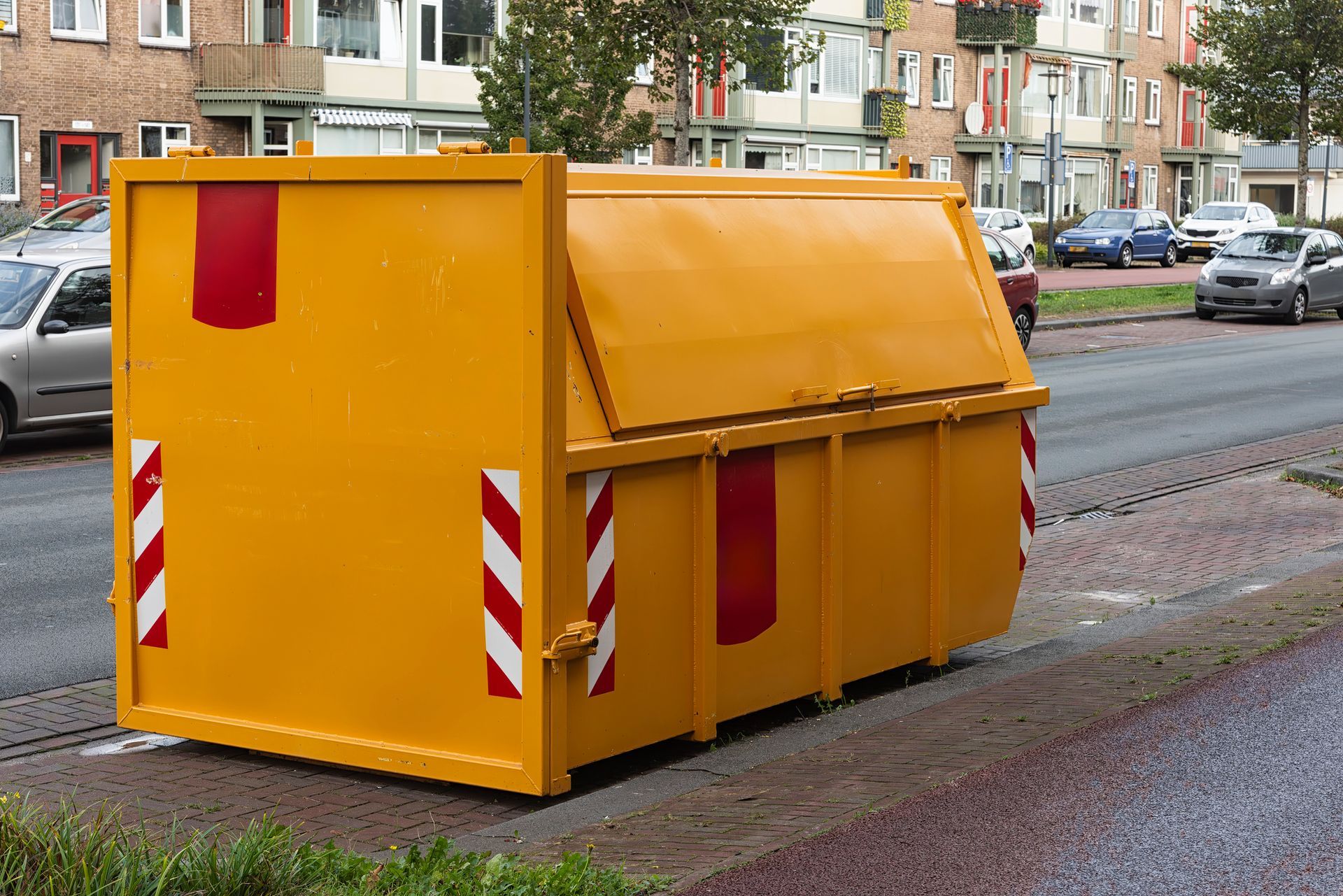 Yellow steel waste container with closed shutters stands outside in a parking lot in a residential a