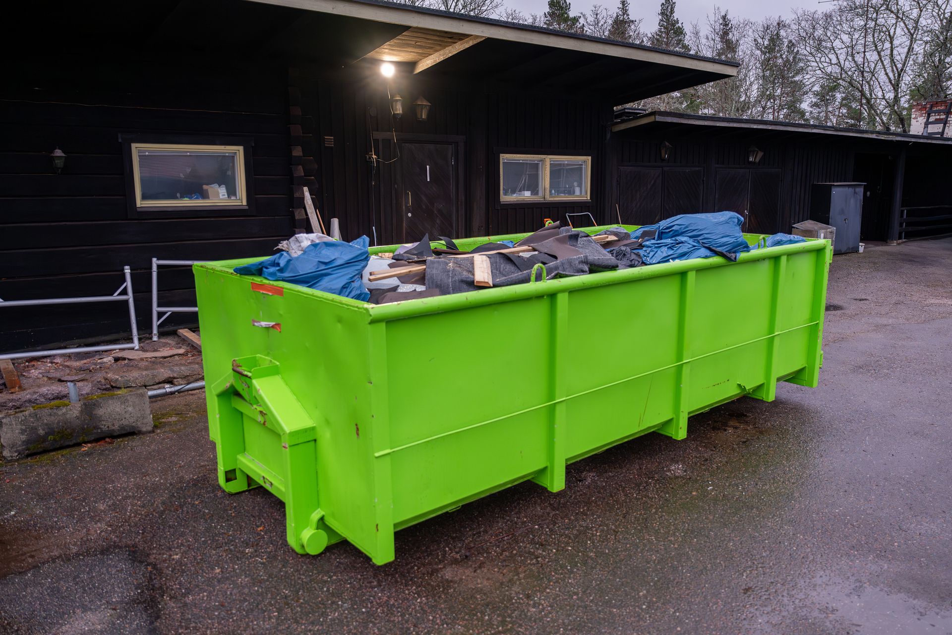 Green dumpster filled with debris beside dark building wall. Green dumpster filled with debris beside dark building wall.