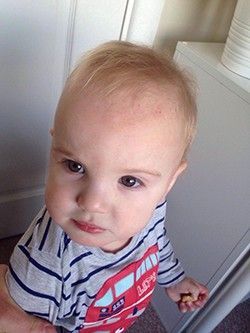 A baby is wearing a striped shirt and looking at the camera.
