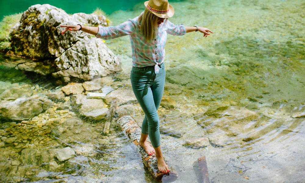A woman is walking barefoot on a rock in the water.