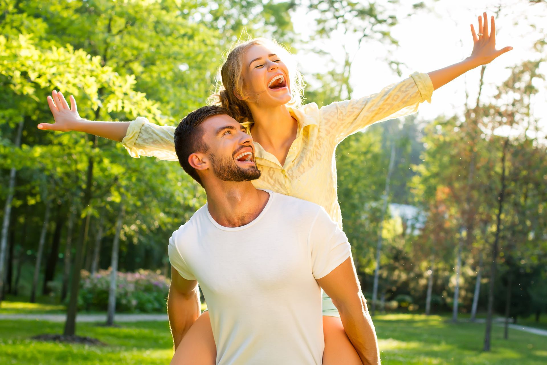 A man is carrying a woman on his back in a park.