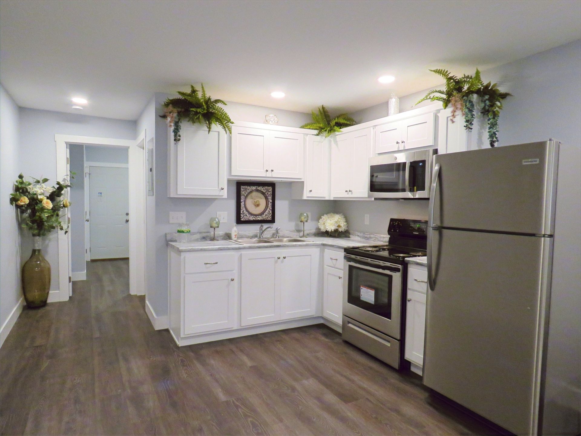 A kitchen with white cabinets , stainless steel appliances , a refrigerator , stove , microwave and sink.