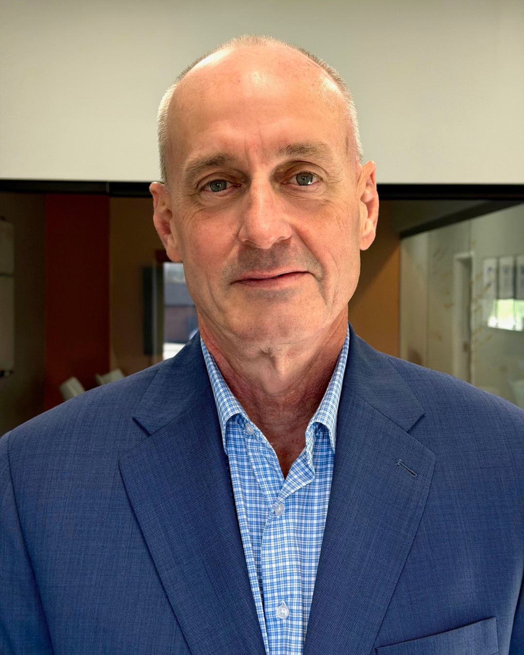 Blond woman in navy blazer smiling against a dark background.