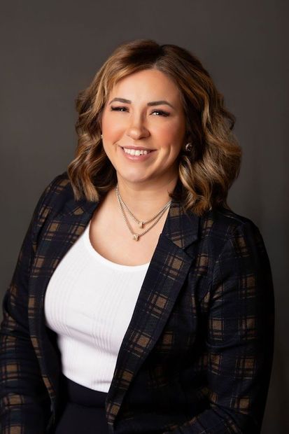 A woman wearing a plaid jacket and a white tank top is smiling for the camera.