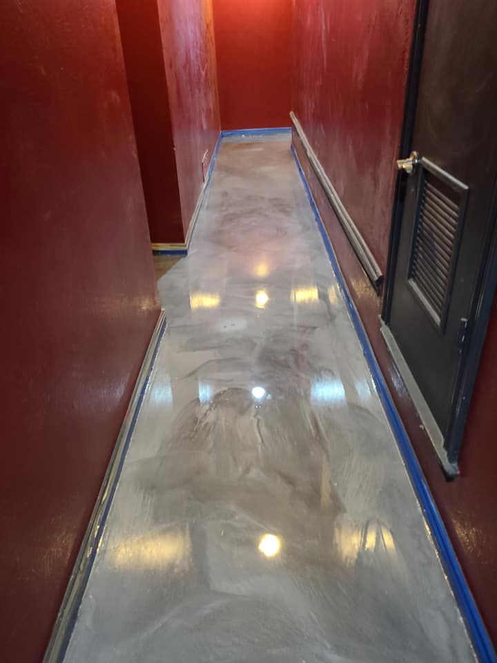 Shiny silver epoxy floor in a narrow hallway with red walls and a dark door.