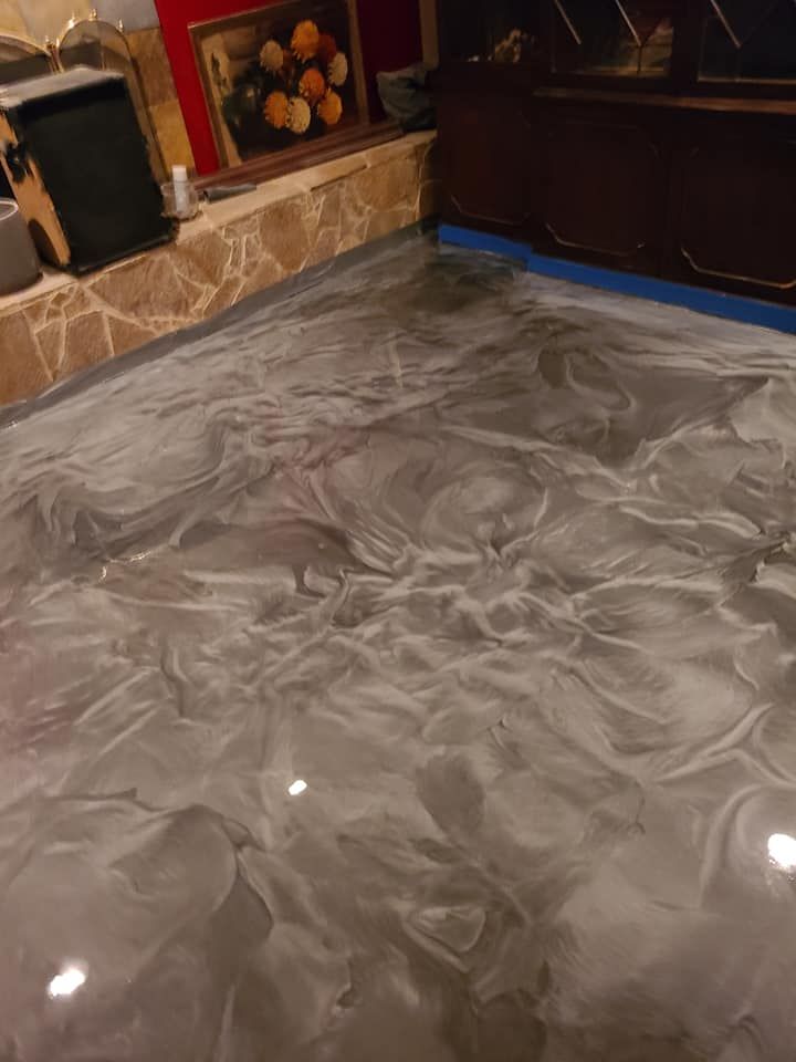 Metallic gray epoxy flooring in a room with textured stone walls and artwork.