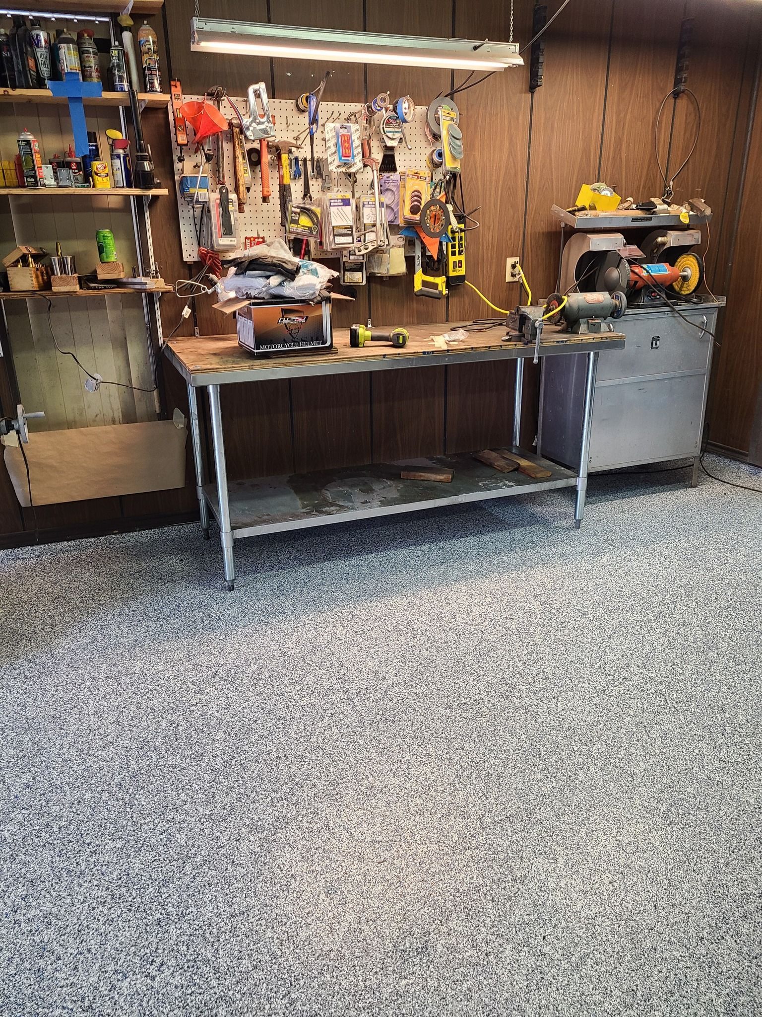 Workshop with tools, workbench, and grinding machine against a wood-paneled wall. Epoxy-speckled floor.