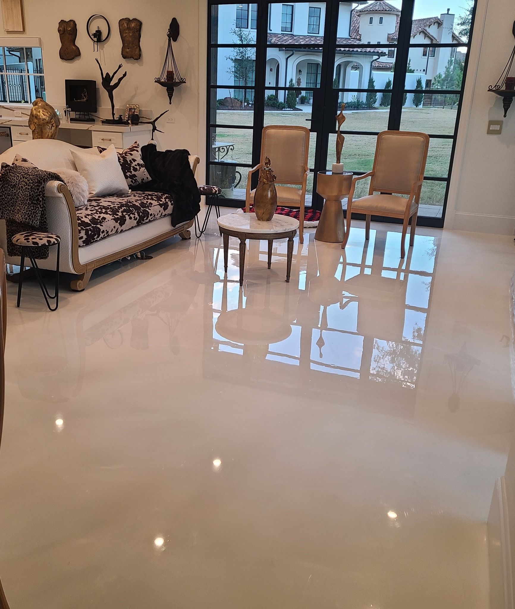 Living room with glossy white floor, elegant furniture, large windows overlooking a lawn.