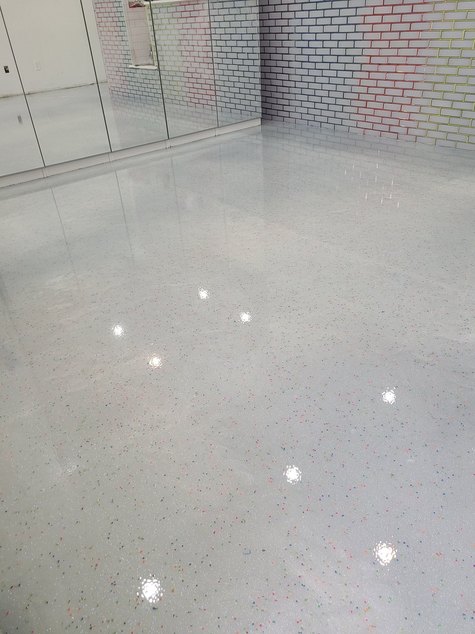 Shimmering gray epoxy floor with embedded glitter, in a room with a textured brick wall and white accents.
