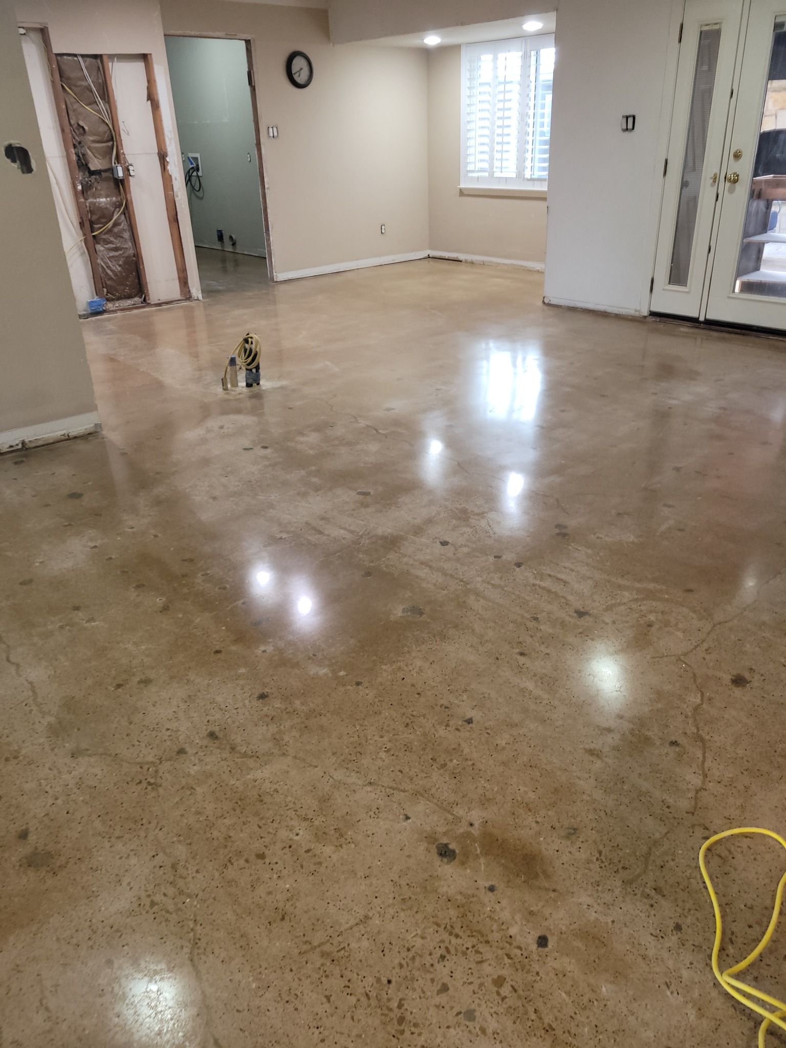 Polished concrete floor in a room under construction. White walls, a door, and a window are visible.