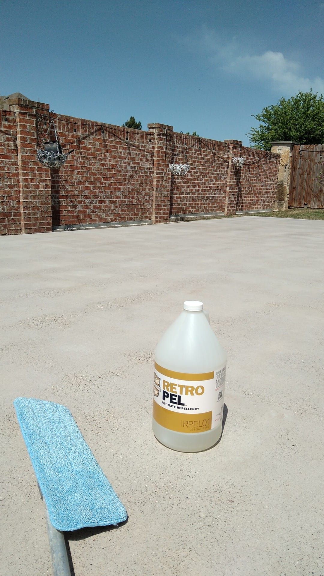 A jug of Retro-Pel cleaner and a mop on a light-colored concrete surface, with a brick wall in the background.