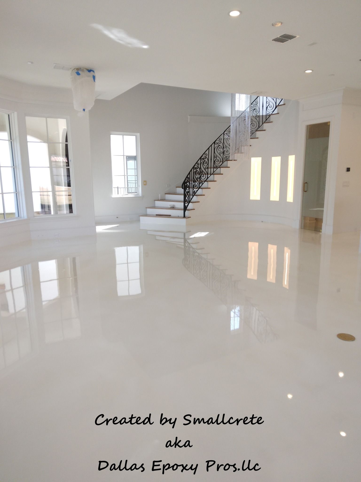White epoxy floor reflecting sunlight in a modern home, leading towards a staircase with a black wrought iron railing.