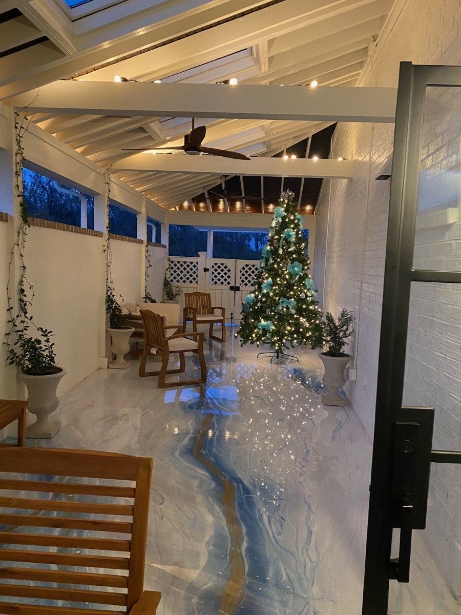 An outdoor patio decorated for Christmas with a tree, lights, and seating. The floor has a blue and white design.