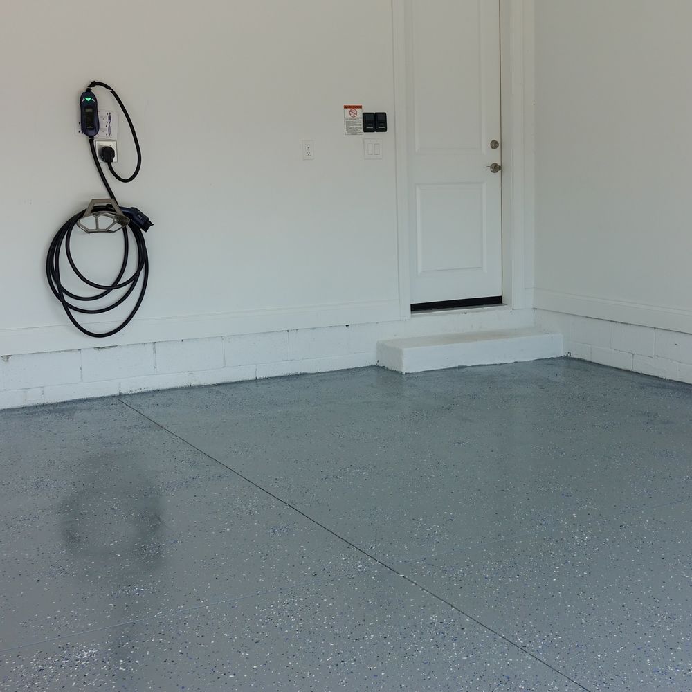 Empty garage with gray epoxy floor and wall-mounted EV charger. A door is at the back.