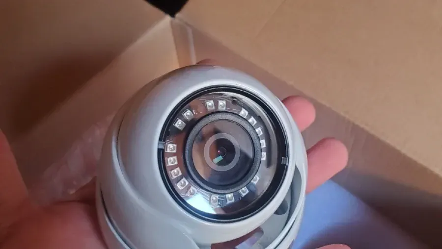 A white dome security camera with a ring of LED lights held in a hand, inside a cardboard box.
