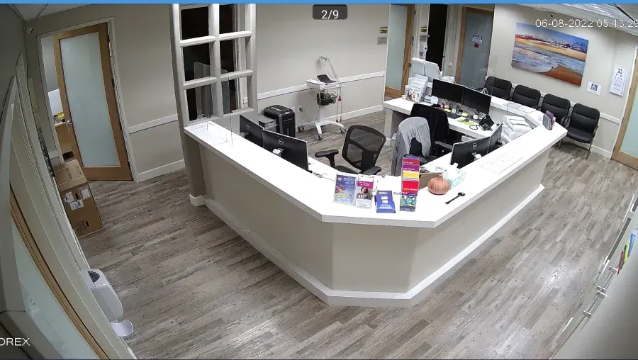 An overhead view of a doctor's office reception area. The desk is white and L-shaped with a person sitting at a computer. There are chairs in the background.