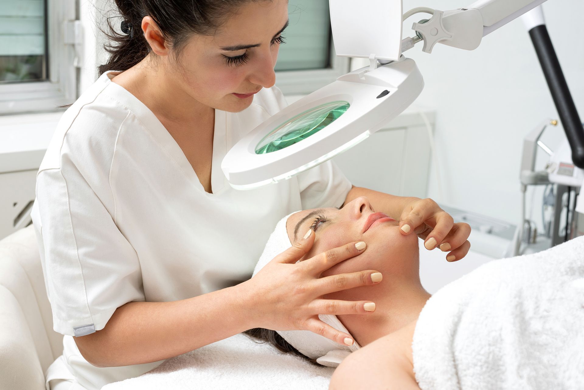 Female cosmetologist doctor analyzing woman’s skin with a magnifying glass during a consultation.