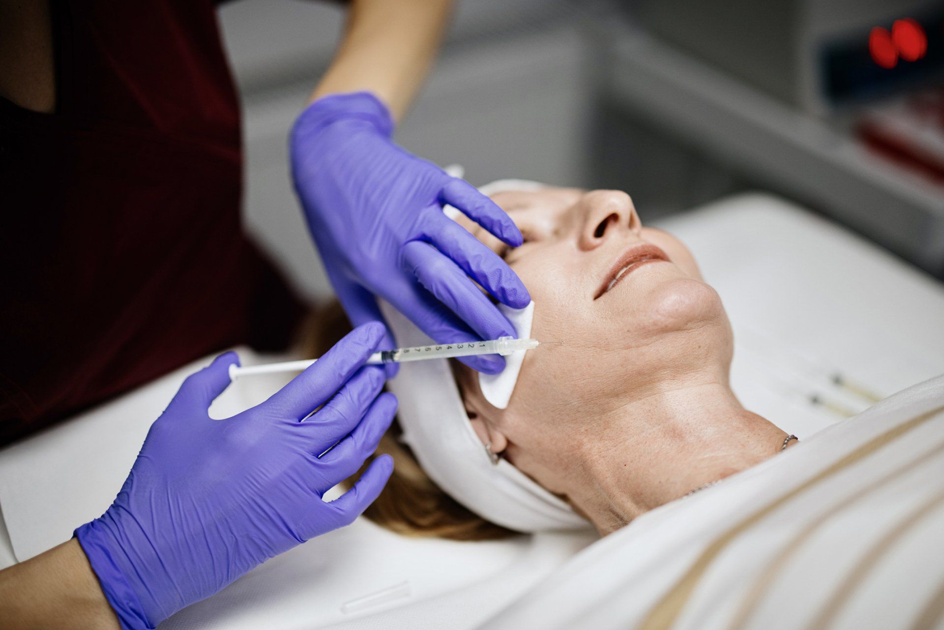 Person receiving facial injections; purple-gloved hands, syringe, clinic setting.