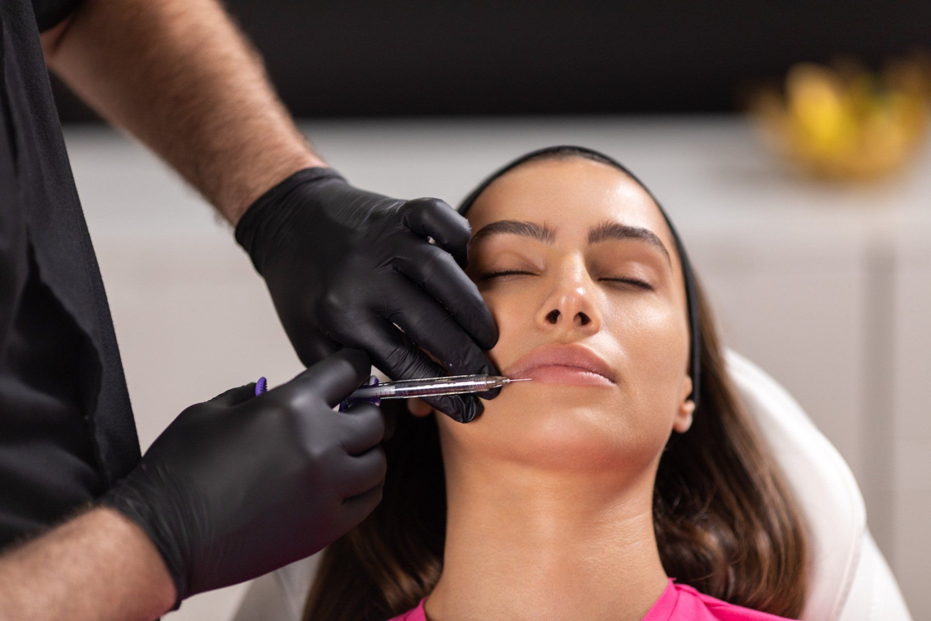 Person receiving lip injections, being administered by someone wearing black gloves.