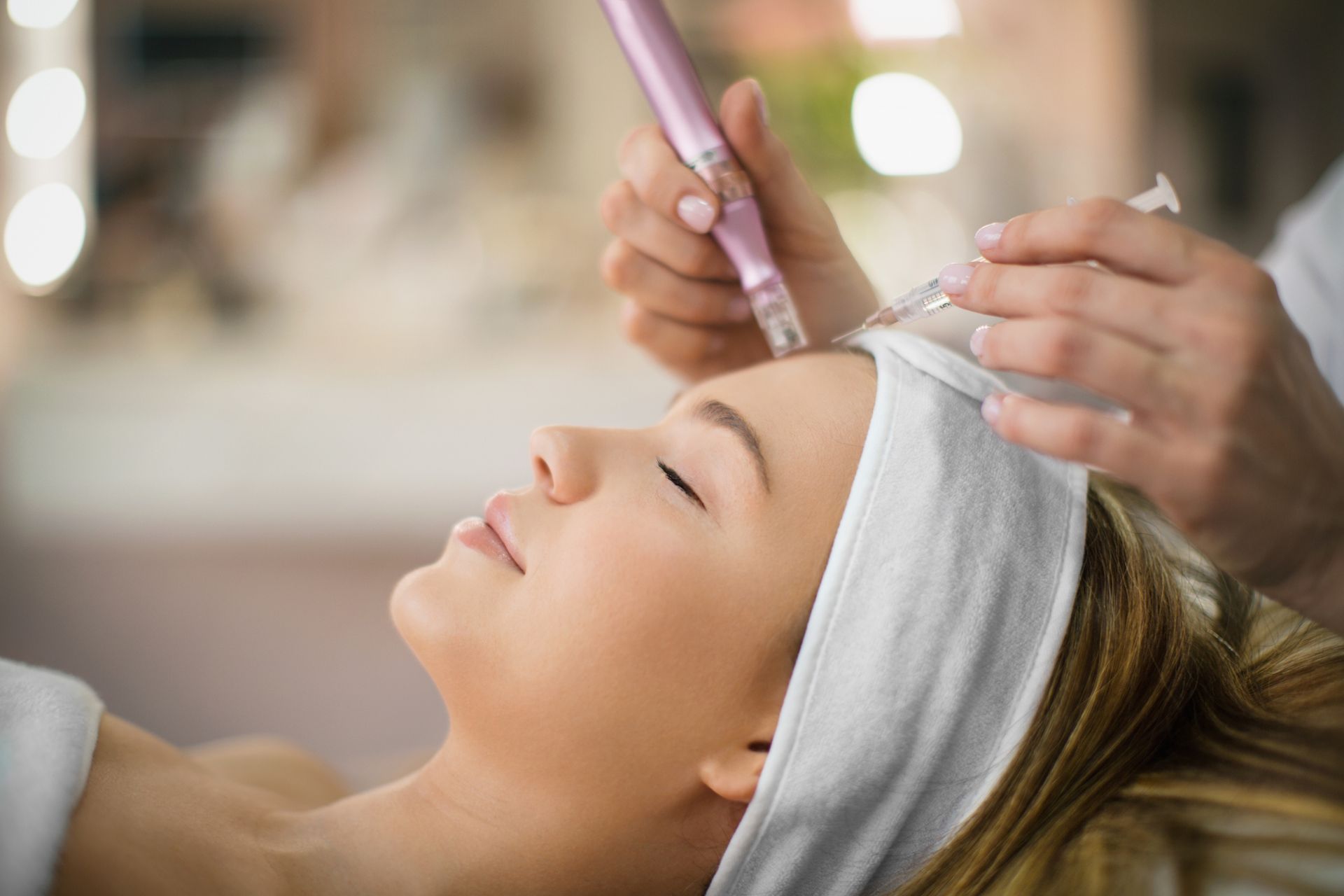 An unrecognizable beautician performs facial treatment on a young woman at a medical spa clinic.