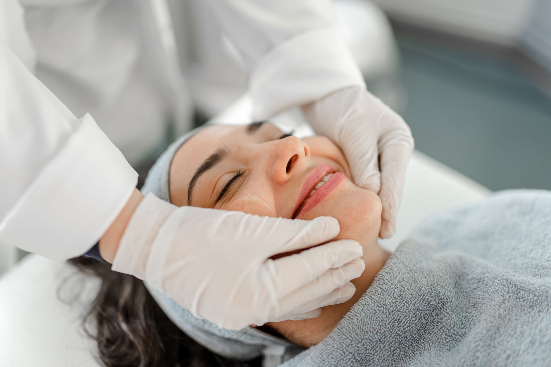 Close-up of a smiling woman receiving an aesthetic medical spa service from an esthetician.