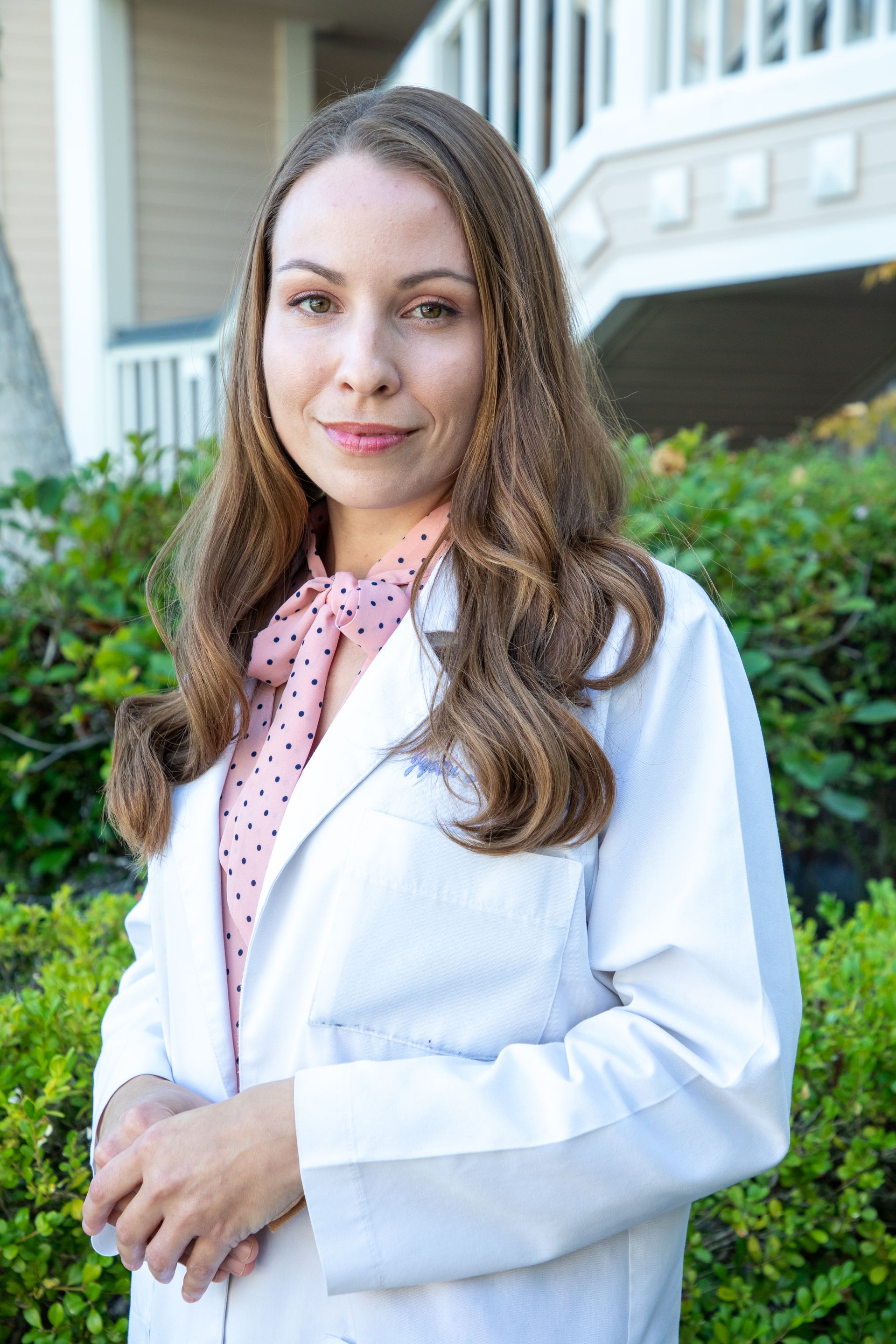 Woman in a white lab coat and polka-dot scarf, standing outdoors.