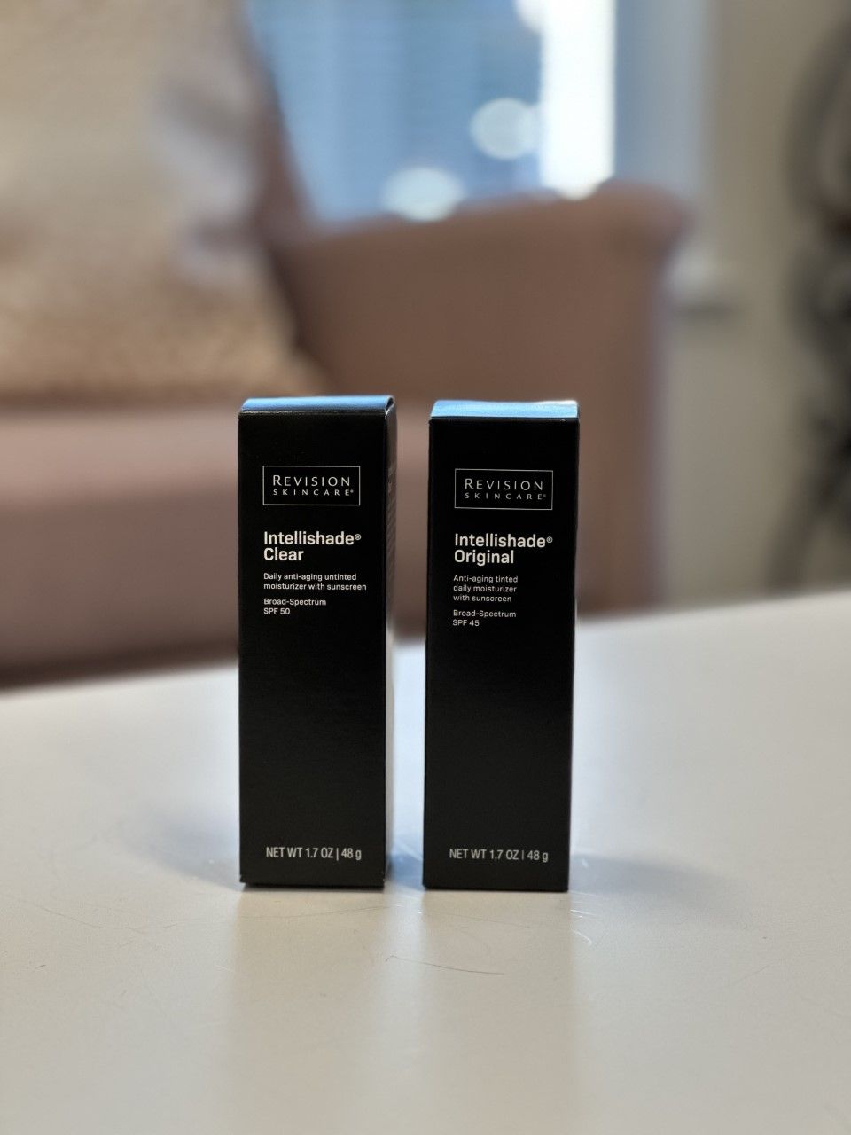 Two black boxes of LaLaLash lash serum on a white surface, with a blurred pink couch in the background.