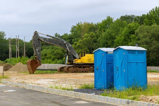 Blue portable restrooms at a construction site with an excavator in the background.