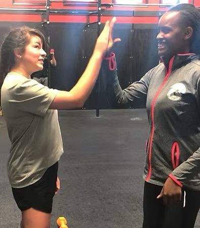 Two people in athletic wear give each other a high-five inside a gym.