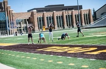 People exercising on a football field in front of a brick building.