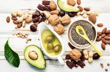Nuts, avocado, olive oil, and chia seeds arranged on a white wooden surface, representing healthy fats.